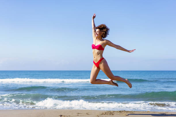 istock Slim woman in bikini jumping on sandy beach 2148736388