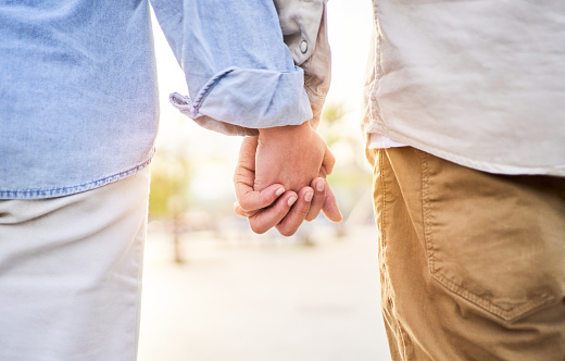 Beautiful close up photo of an unrecognizable caucasian couple holding hands outside against the sunlight. Copy space.