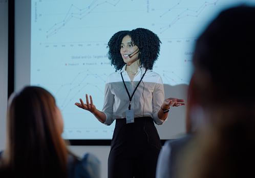 Woman, finance and workshop with presentation by board for stats, growth and stock market with audience. Person, presenter and financial advisor with charts, speech or projector overlay at trade show