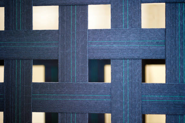 Wide strips of thick blue fabric are intertwined with each other. Grid background of blue lines. Sturdy fabric base for mattress close-up blue color