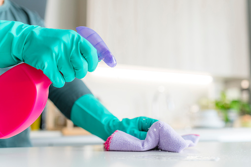 Close up view of hand wearing washing up gloves, spray cleaner bottle and rag cleaning kitchen surface. High resolution 42Mp indoors digital capture taken with SONY A7rII and Zeiss Batis 40mm F2.0 CF lens