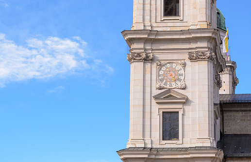 Part of the Salzburg Cathedral with a clock against a background of blue sky with cloud in horizontal format