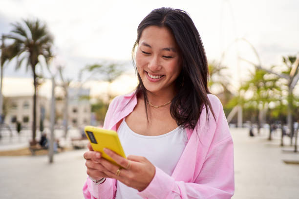 istock Cheerful Chinese woman using phone to send online text while walking outdoors. 2148739736