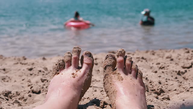 POV Female Wet Feet in Sand Lying on a Sandy Beach in Sun Glare near the Sea