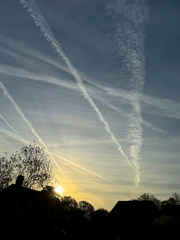 Vapour trails in the early morning behind a silhouetted house and trees