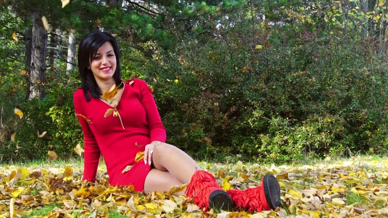 Young Woman In A Red Dress Sitting On The Grass In A Park In Autumn