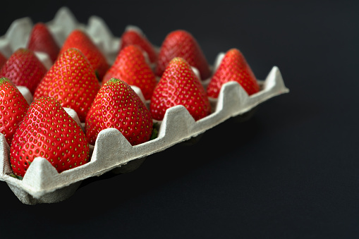 Lots of ripe strawberries in a cardboard box on a bleack background with free spase on the right