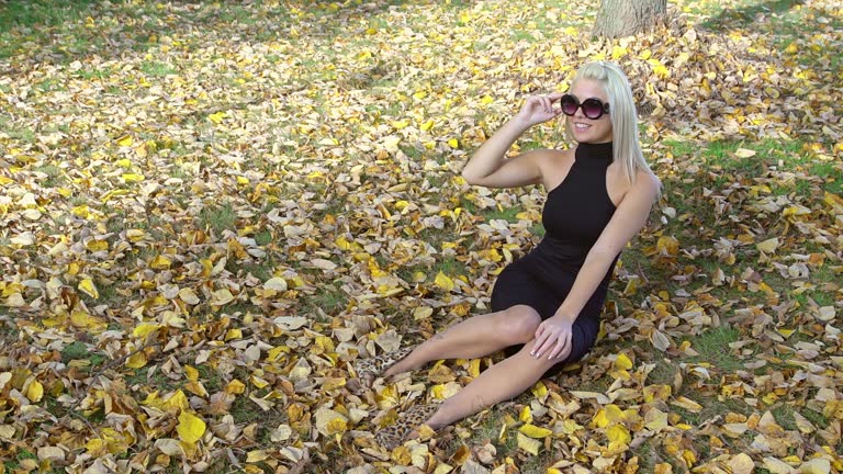 Young Woman In A Black Dress Sitting On The Grass In A Park In Autumn