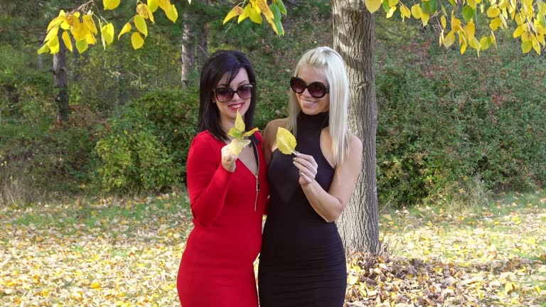 Two Female Friends Holding Autumn Leaves In A Park