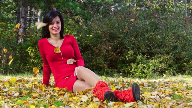 Young Woman In A Red Dress Sitting On The Grass In A Park In Autumn