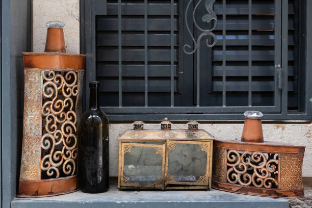 A broken down, dirty glass housing with brass doors for a Hanukkah menorah set on a window sill along with a bottle and two worn, metal containers.