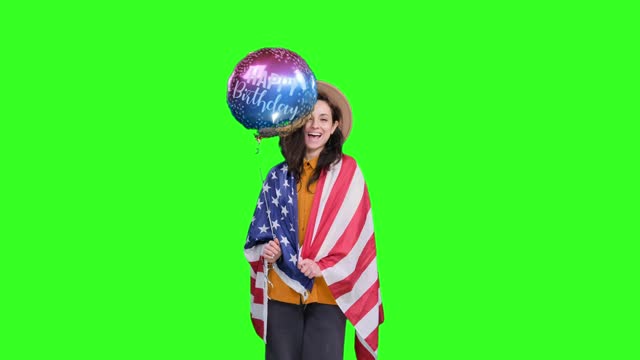 Happy woman draping USA flag and holding birthday balloon on the chroma key