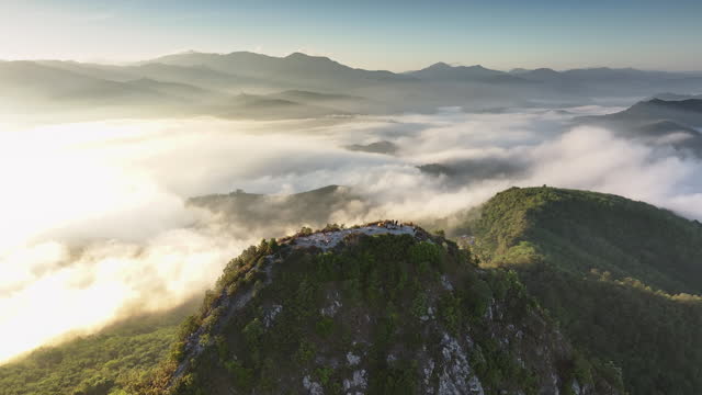 Aerial fly orbiting around mountain peak revealing sunrise over the sea of mist