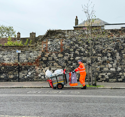 A street cleaner in high viz clothing picks up litter on a street in the town of Sandwich in Kent. April 2024