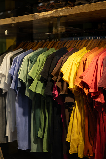 Colorful T-shirts on wooden hanger hanging on clothing rack in the store. Clothing, style, shopping concept.