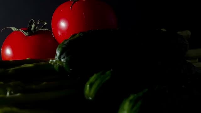 Small tomatoes, cucumbers and asparagus pods rotate on a white plate on a dark background. Food shooting.