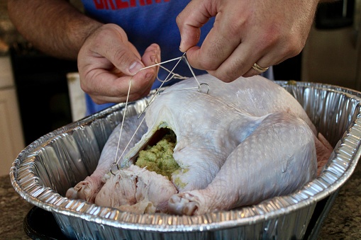 A man is sewing a turkey shut after stuffing it.
