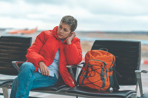 Traveler using phone, sitting in an airport, waiting for a flight, walking inside an airport, Carrying a backpack. Travel concept