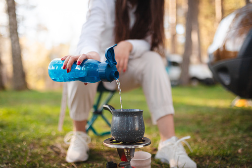 Close-up of an unrecognizable woman making coffee while camping in nature.