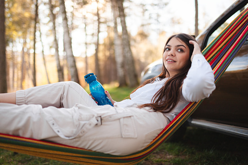 Beautiful young woman laying in a hammock while camping in a forest.