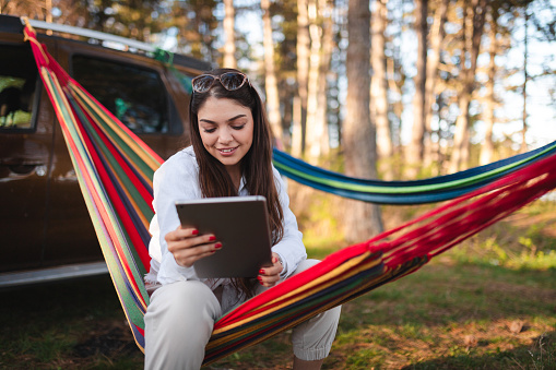 Young woman using a tablet while sitting in a hammock outdoors.