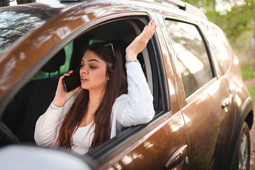 Stressed young woman calling for help while sitting in her car.