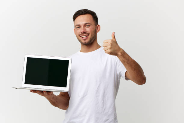 istock Joyful smiling tanned handsome IT professional man in white basic t-shirt hold laptop show thumb up posing isolated on white studio background. Copy space Banner Mockup. Electronics repair concept 2148748781