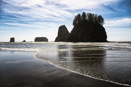 Silhouetted sea stacks with trees atop on Second Beach, La Push with sparkling reflections known as a glitter pattern and dynamic sky in Washington State, photographed against the sun.