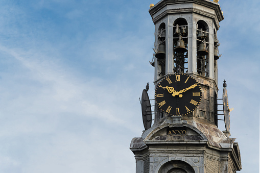 Munttoren Clock Tower, Amsterdam, against a blue sky. Tower has a large clock face and a weathervane at the top. Background, space for text, copy space