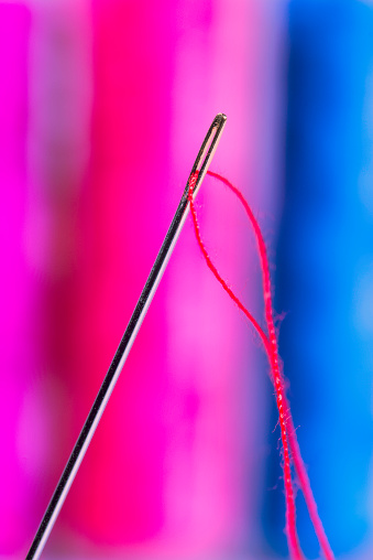 Close-up view of one needle with red thread with differently colored spools of thread on background