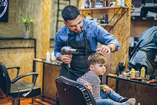 Little boy getting a haircut by barber while sitting in chair at barbershop