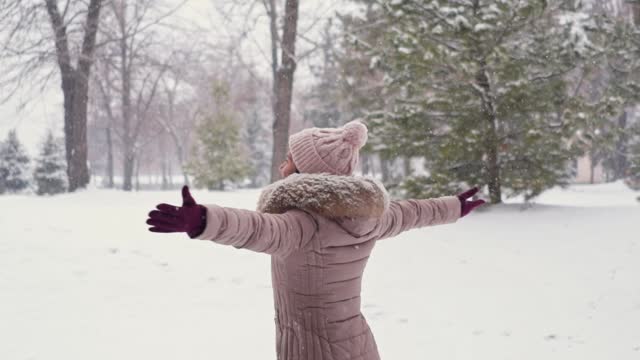 Young Woman Spinning Around Happily In A Snowy Park In Winter