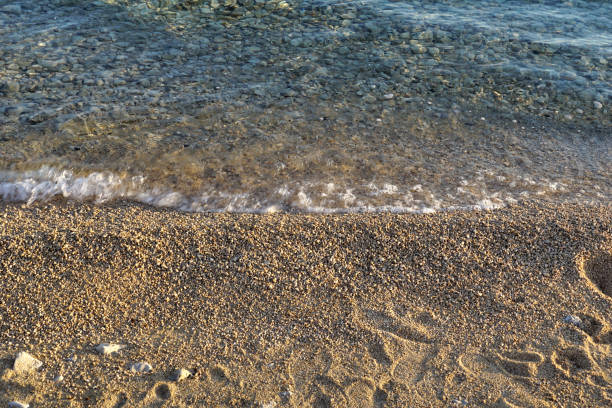 Transparent sea water next to a pebble beach with footprints beetween pebbles