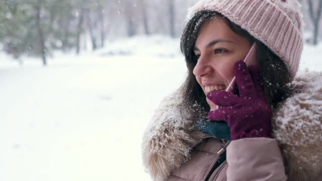 Young Happy Woman Talking On A Phone In A Snowy Park In Winter