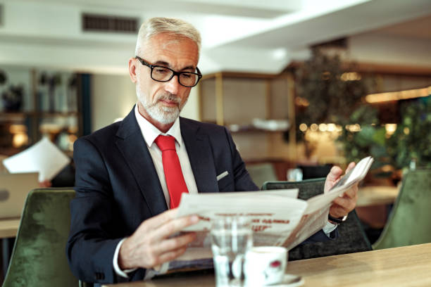 istock Well dressed senior businessman reading newspaper at cafe 2148751463