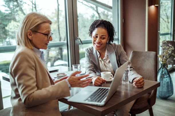 Two female colleagues using laptop during coffee break at the restaurant