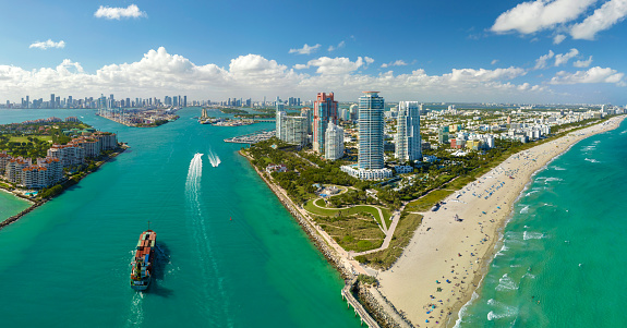 View from above of big container ship entering main channel in Miami harbor near South Beach high luxurious hotels and apartment buildings.