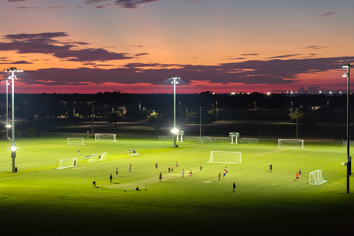 People playing soccer game on illuminated public stadium at sunset. Active way of life concept.
