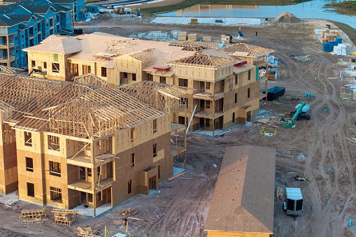 Development of residential housing in American suburbs. Unfinished frames of apartment condos with wooden roof beams under construction. Real estate market in the USA.