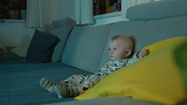 Adorable Baby Boy Sitting On Sofa Watching TV At Home