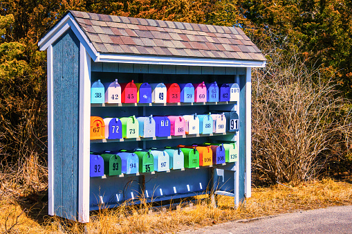 Rows of colorful numbered mailboxes in a built shingled shed along a Cape Cod roadway.
