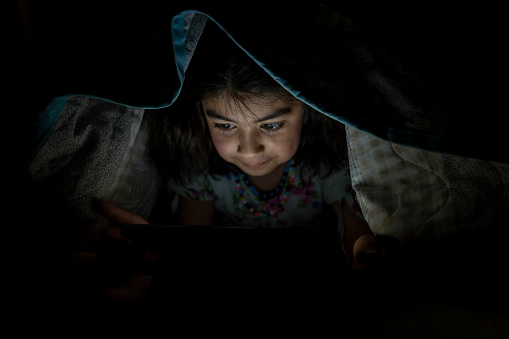 Girl using tablet in bed. Girl lying in bed at night watching video.