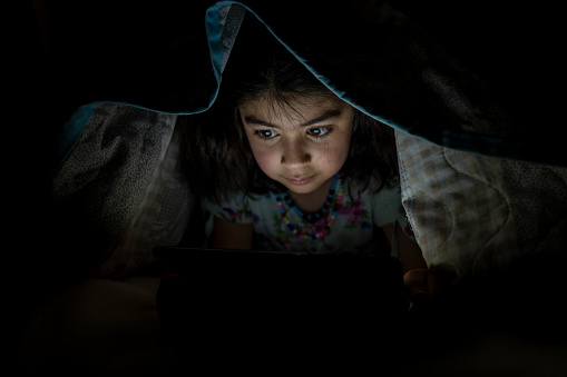 Girl using tablet in bed. Girl lying in bed at night watching video.
