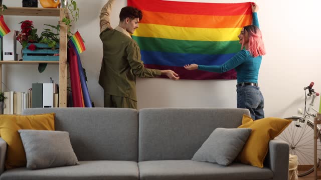 diverse friends placing rainbow flag on wall - preparing lgbt gay pride party