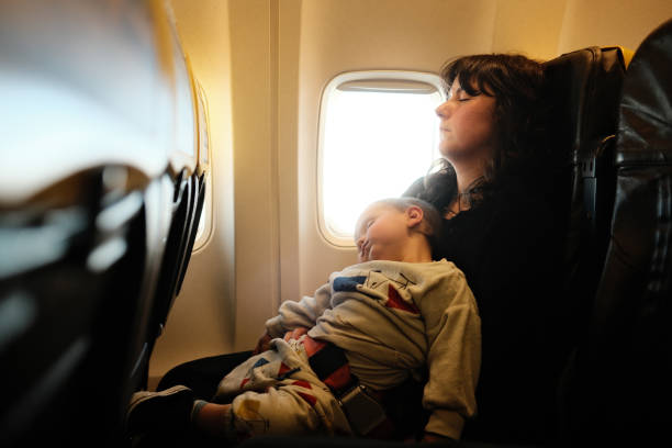 A little boy is sleeping with his mother during a flight. They are embracing together.