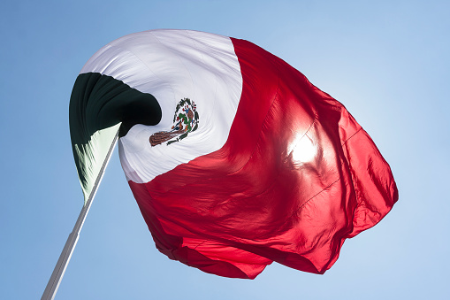 Mexican flag waving in the wind under a blue sky, national symbol of Mexico