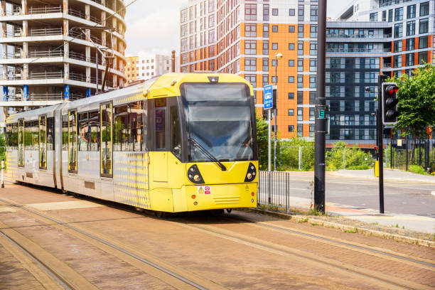 Yellow tram on a tramway running through a new suburban district on a sunny summer day. An apartment building under construction is in background. Salford Quays, Manchester, England.