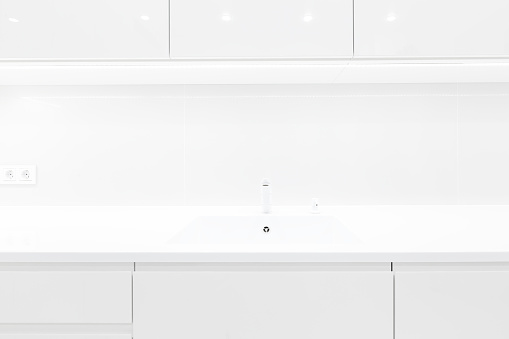 Front view of modern trendy snow white kitchen interior with acrylic countertop and built in acryl sink, luxury monochrome design, image with selective focus