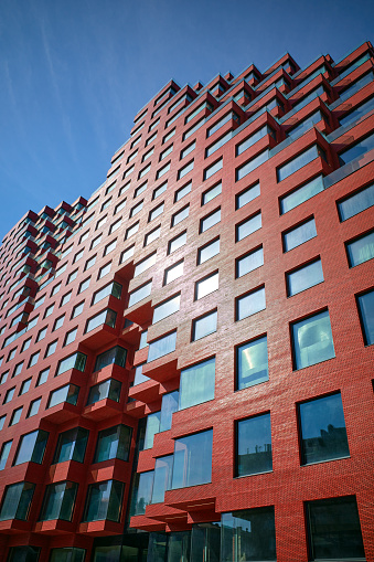 Part of a multi-story abstract red office building from below, blue sky.