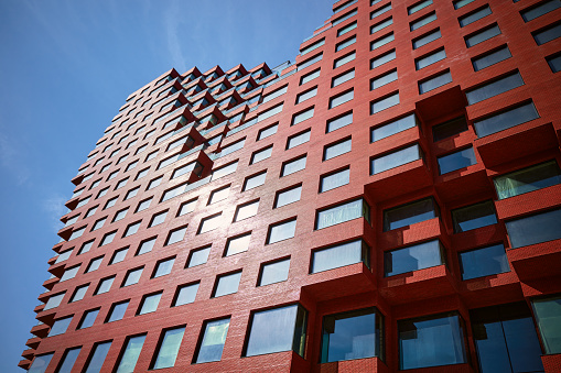 Part of a multi-story abstract red office building from below, blue sky.